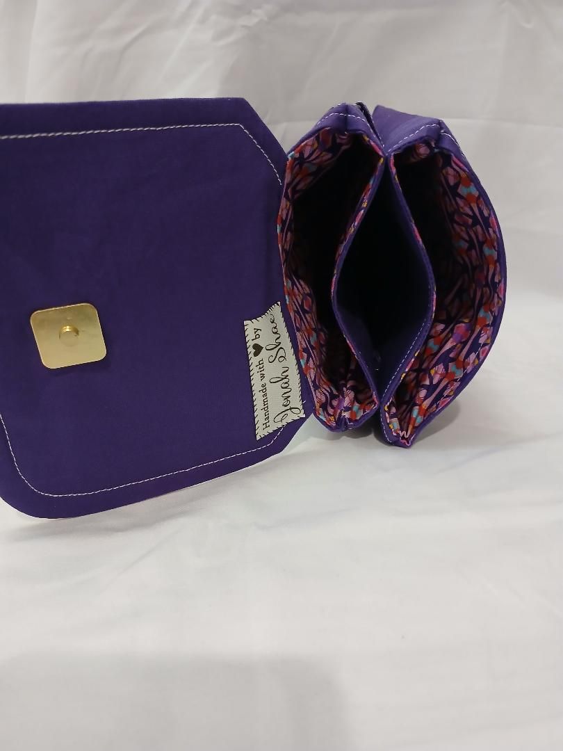 Purple purse with open patterned interior and gold clasp on a white surface