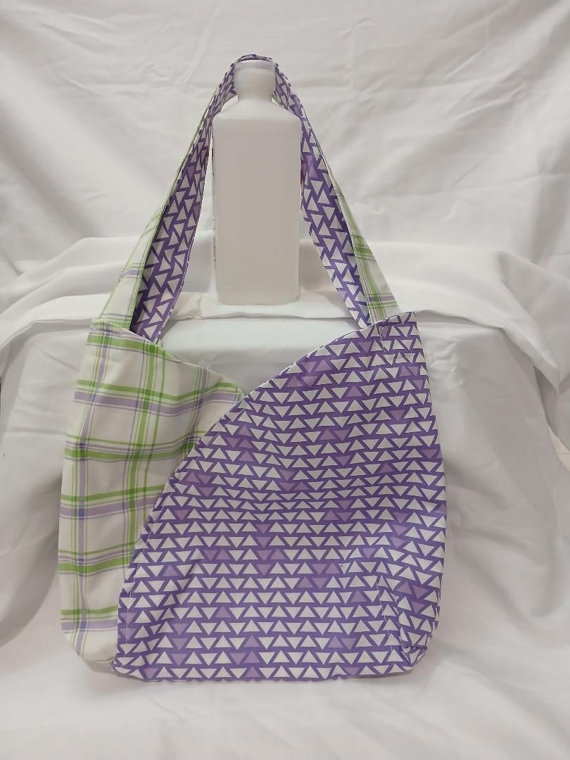 Two patterned tote bags, one purple triangle print and one green plaid, hanging on a white display.