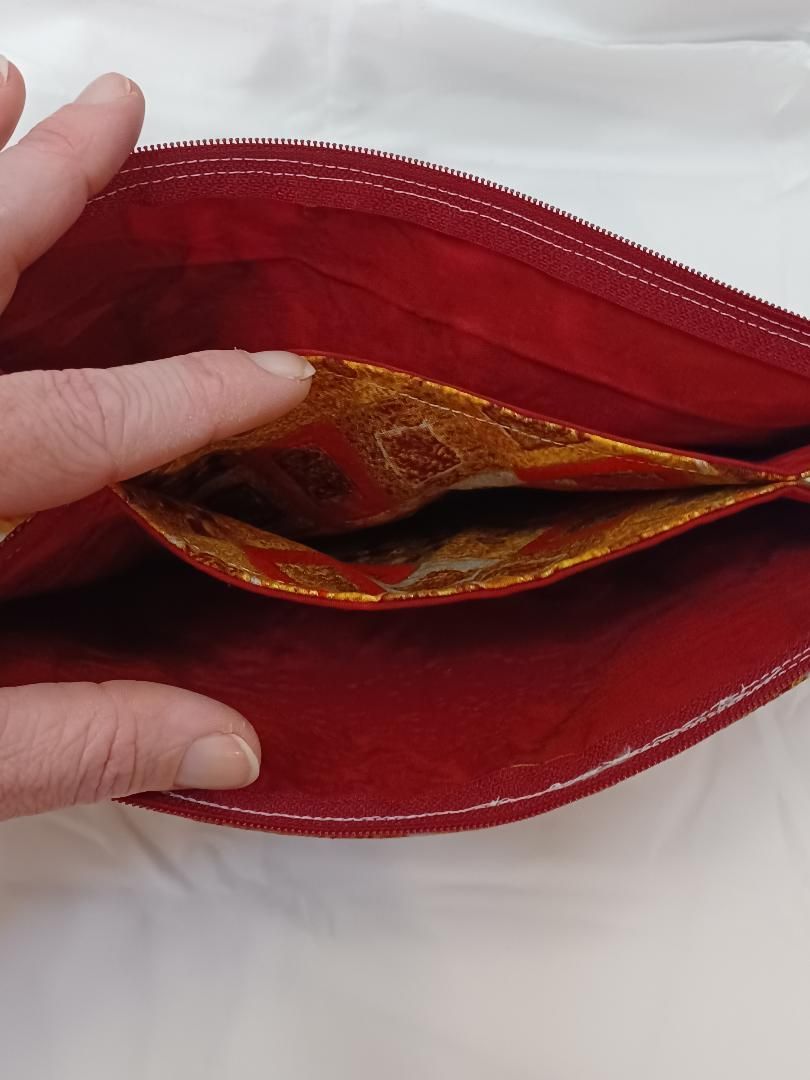 Hand holding open a red zippered pouch with a gold-patterned lining