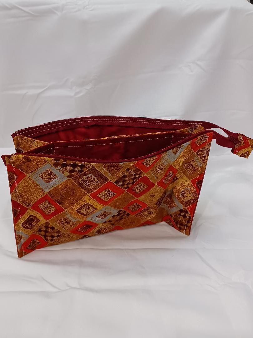 Red and gold patterned zippered pouch on a white fabric background