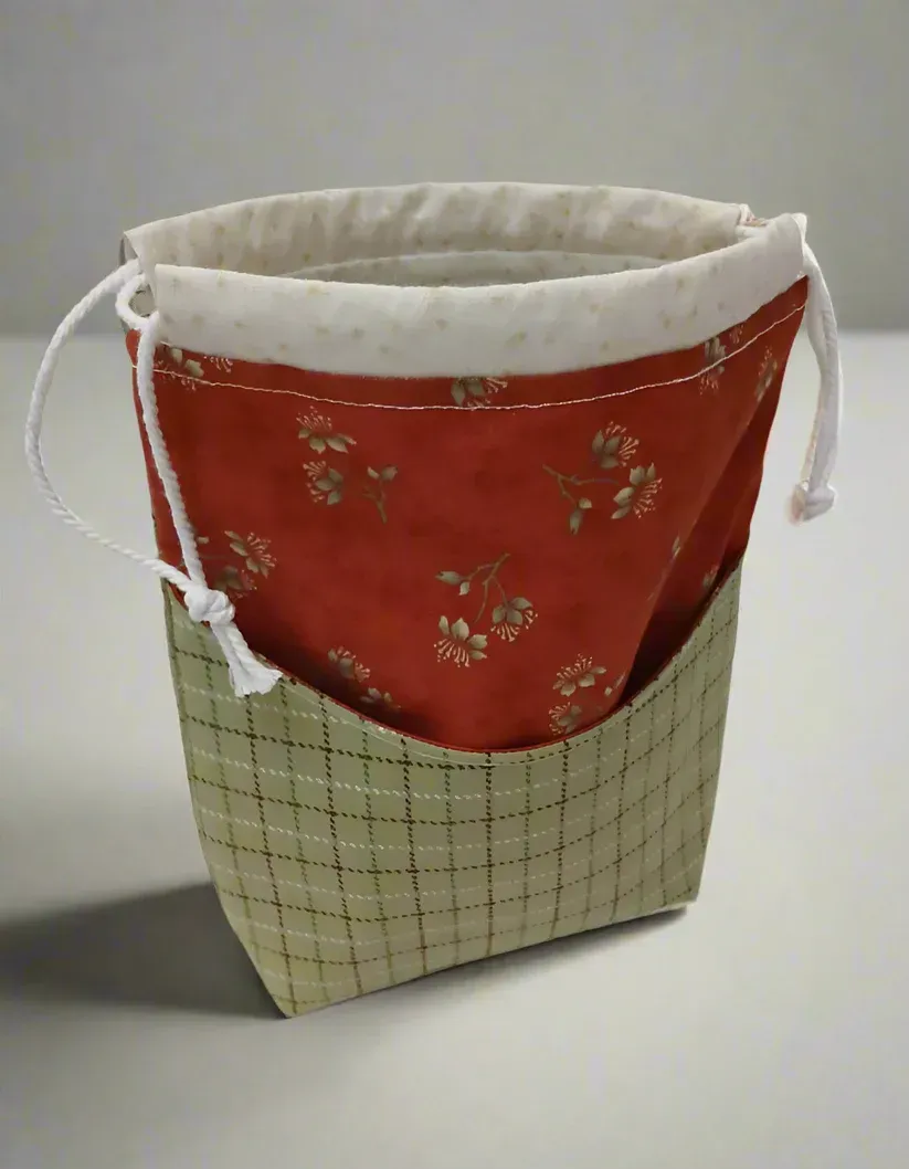 Small red and beige fabric drawstring pouch with white lining, standing upright on a white surface.
