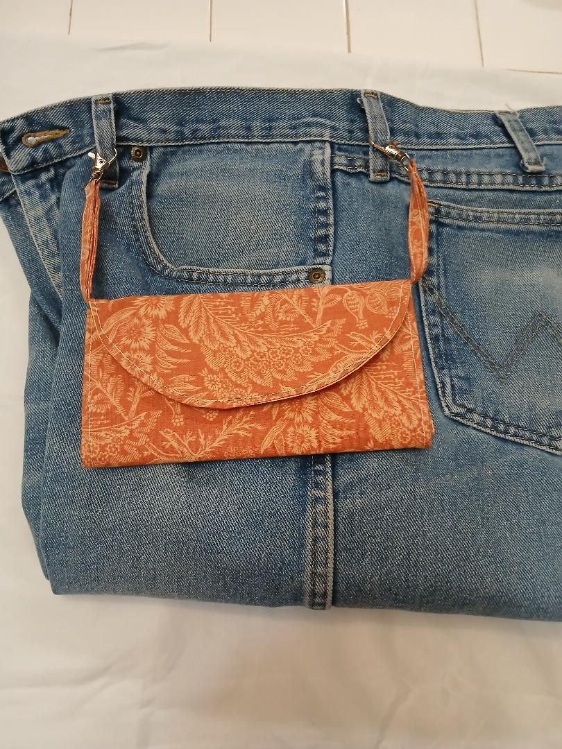 Blue denim bag with orange patterned flap and straps on a white bedspread