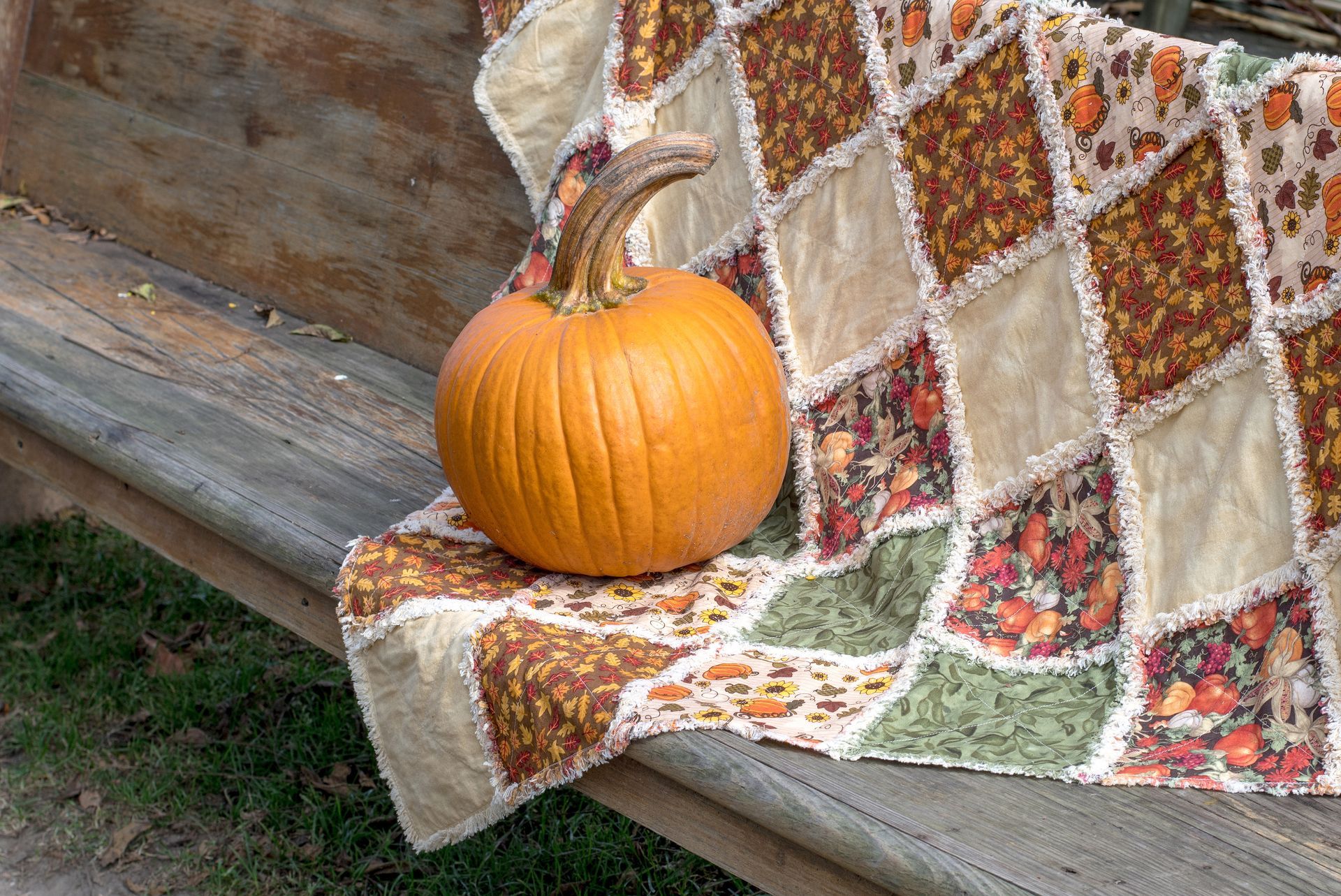 Small orange pumpkin on a patterned quilt draped over a wooden bench outdoors