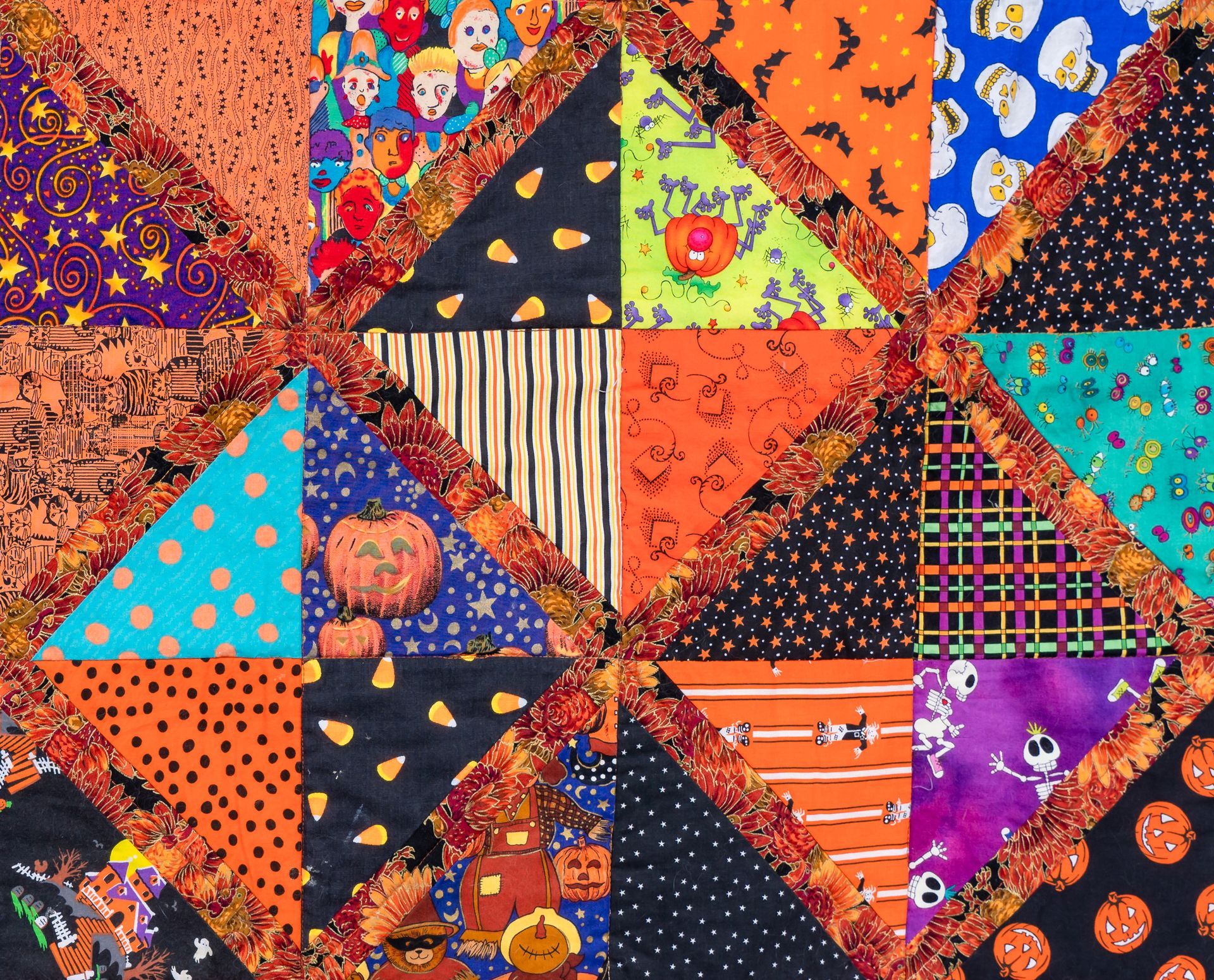 Patchwork quilt of colorful triangular fabric pieces in orange, purple, blue, and black patterns