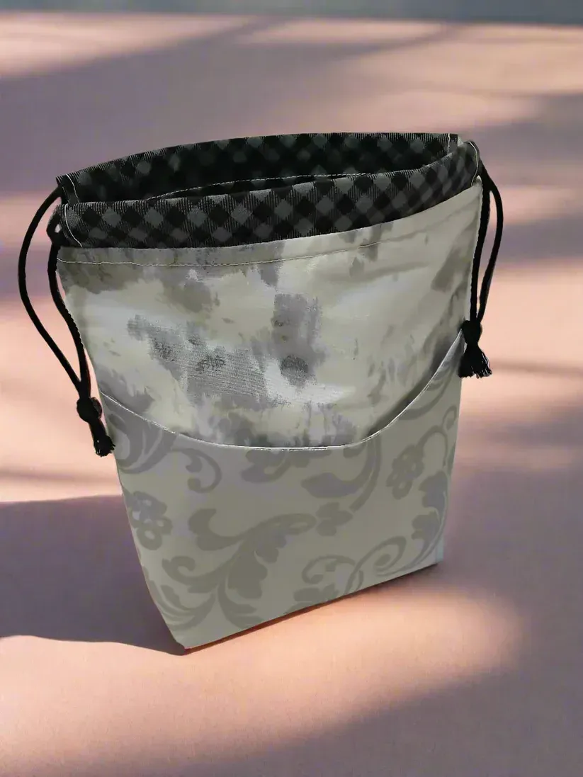 Small patterned drawstring pouch with a dark checkered lining standing on a sunlit surface