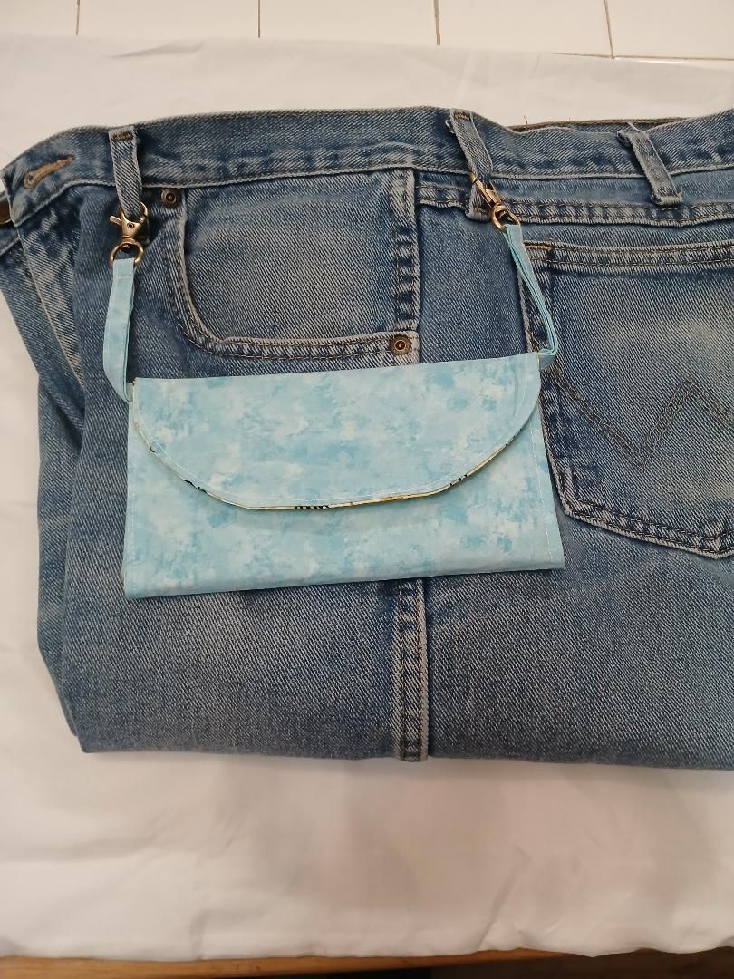 Blue denim jeans with a light blue flap pocket laid flat on a white surface