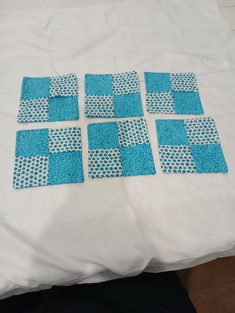 Six small blue-and-white patterned fabric squares arranged in two rows on a white bedspread.