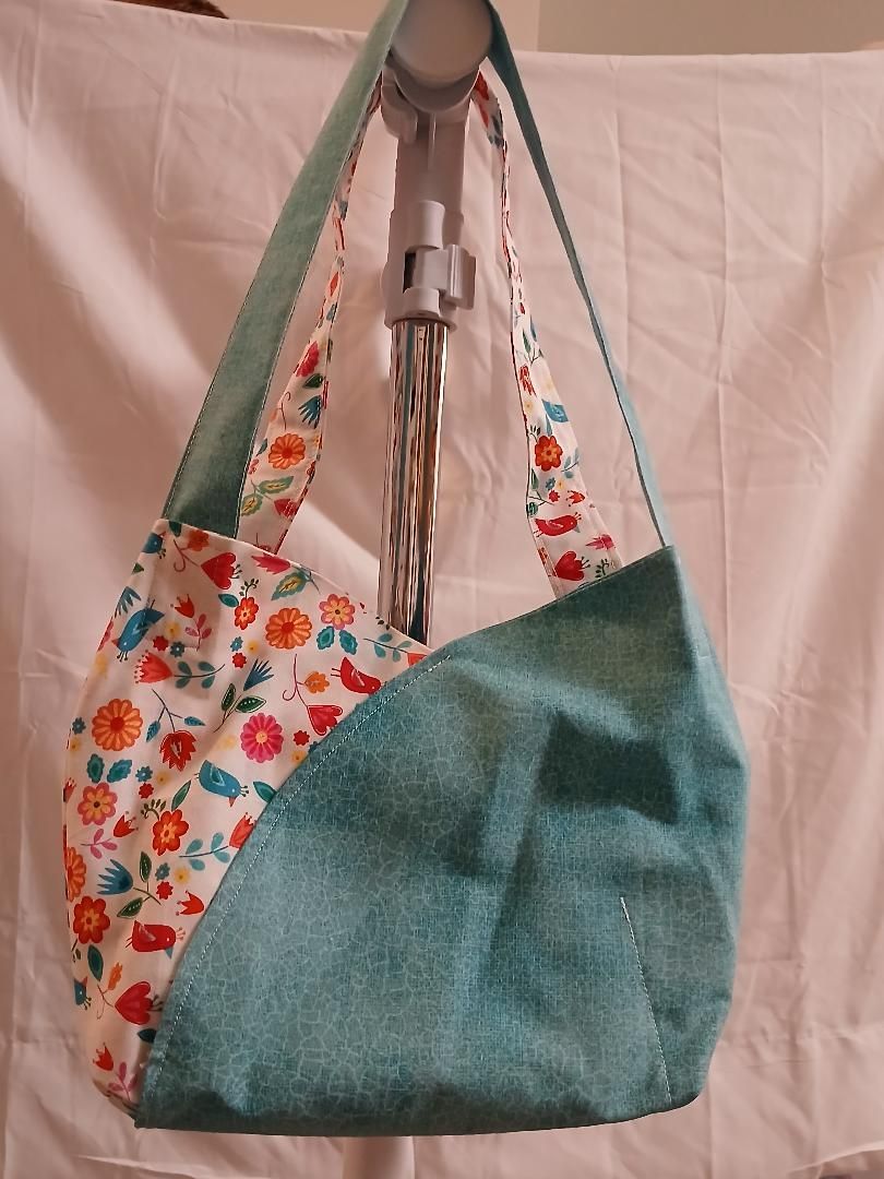 Teal and floral patchwork shoulder bag hanging on a metal rack against a pink background