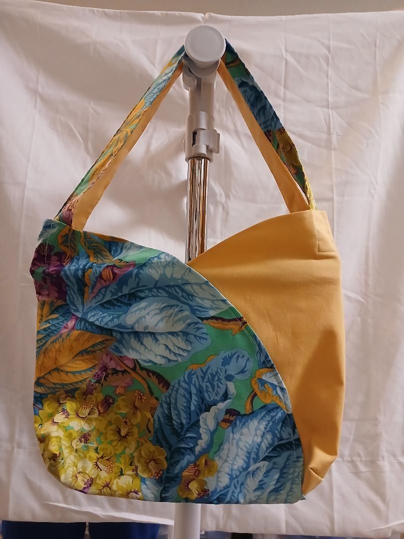 Colorful floral tote bag and yellow bag hanging on a hook against a white backdrop
