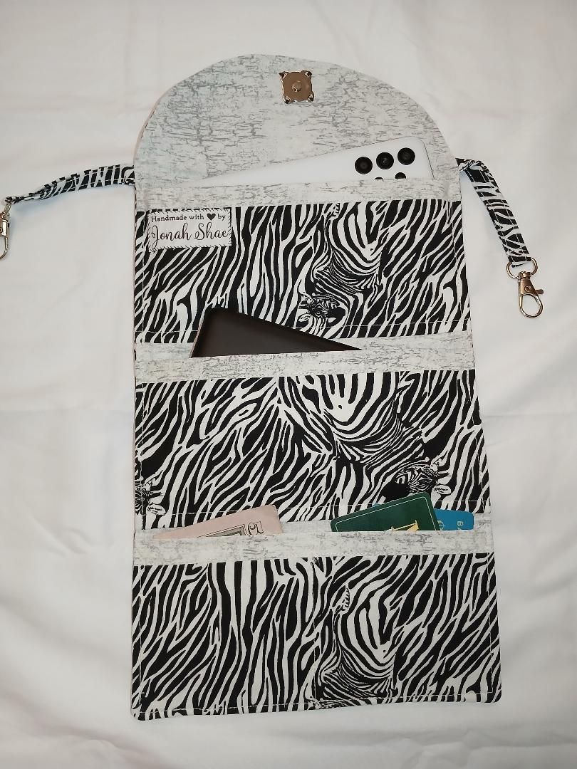 Zebra-print backpack with white top, gray straps, and brown hanging loops on a plain background