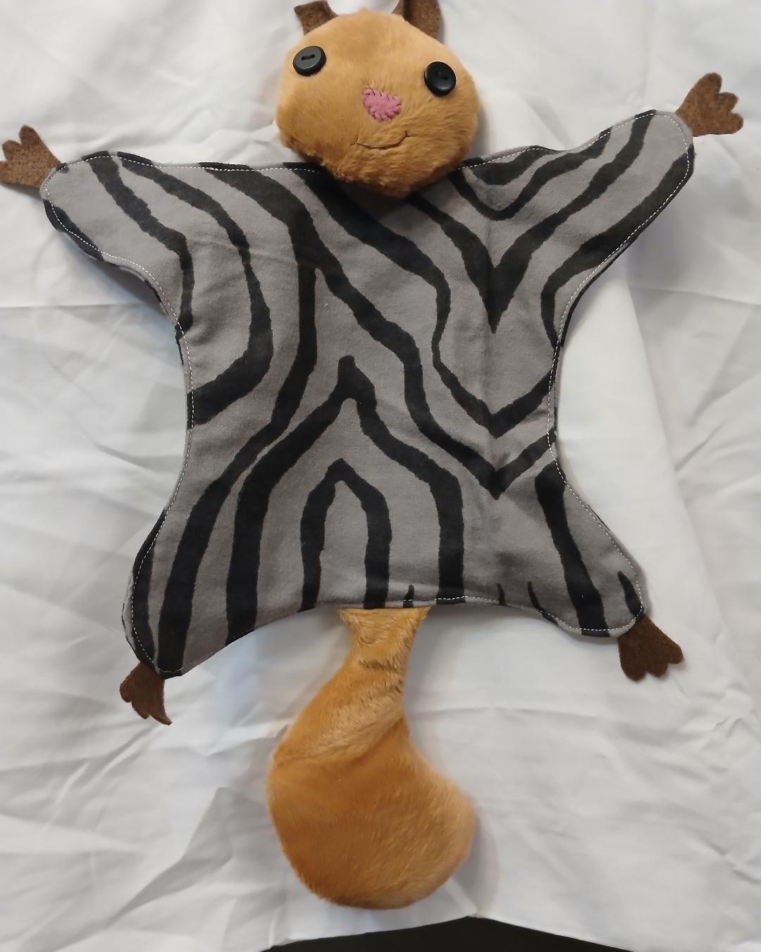Stuffed animal with zebra-striped body, tan head and tail, lying on a white bed
