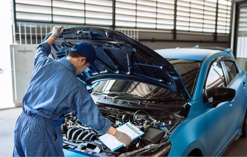 Mechanic inspecting engine of a blue car with the hood open in a garage