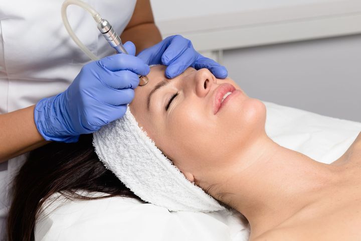Woman receiving a facial treatment with a tool on her forehead, blue gloves visible.