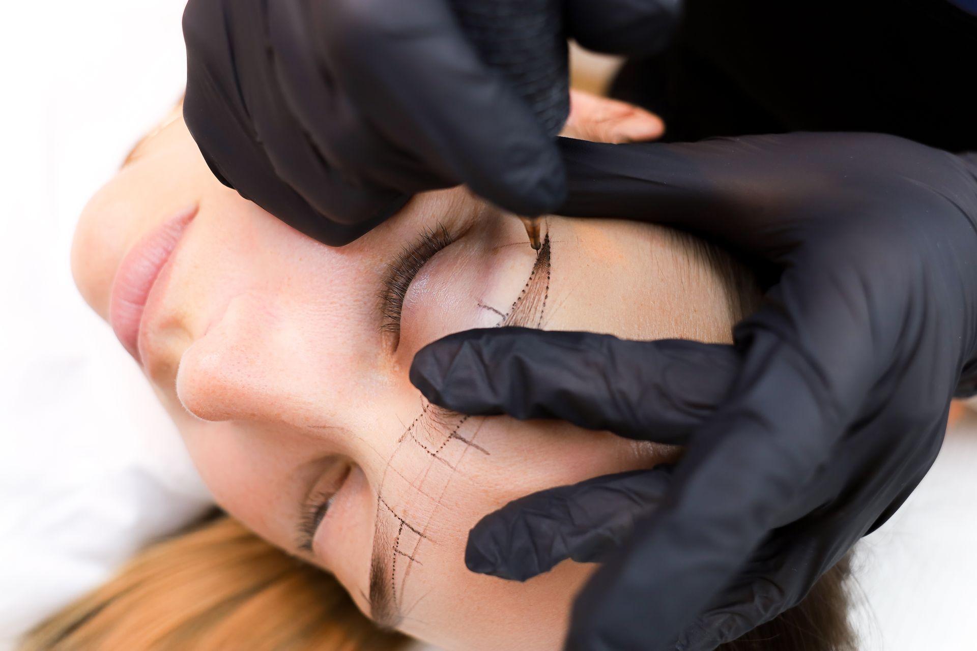 A person getting their eyebrow makeup done by another person with a thin brush, indoors.
