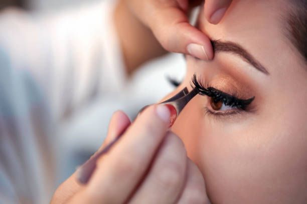 Applying false eyelashes with tweezers. Close-up of eye, person's hand holding tweezers.
