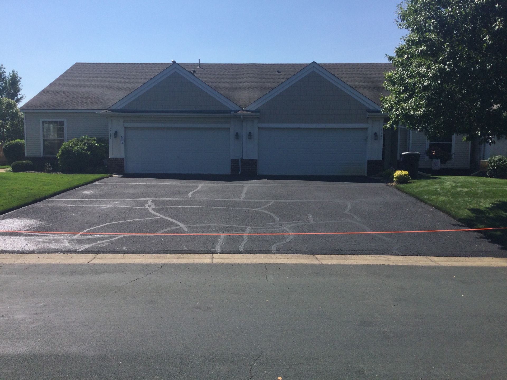 Driveway with cracks in front of a two-door garage and a beige home under a blue sky.