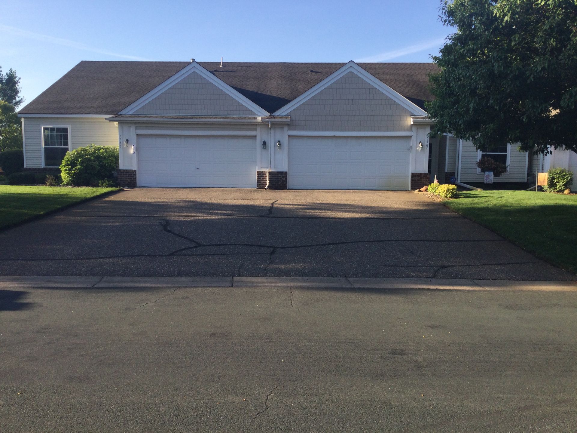 Two-car garage townhouse with white doors, gray asphalt driveway, and green lawn on a sunny day.
