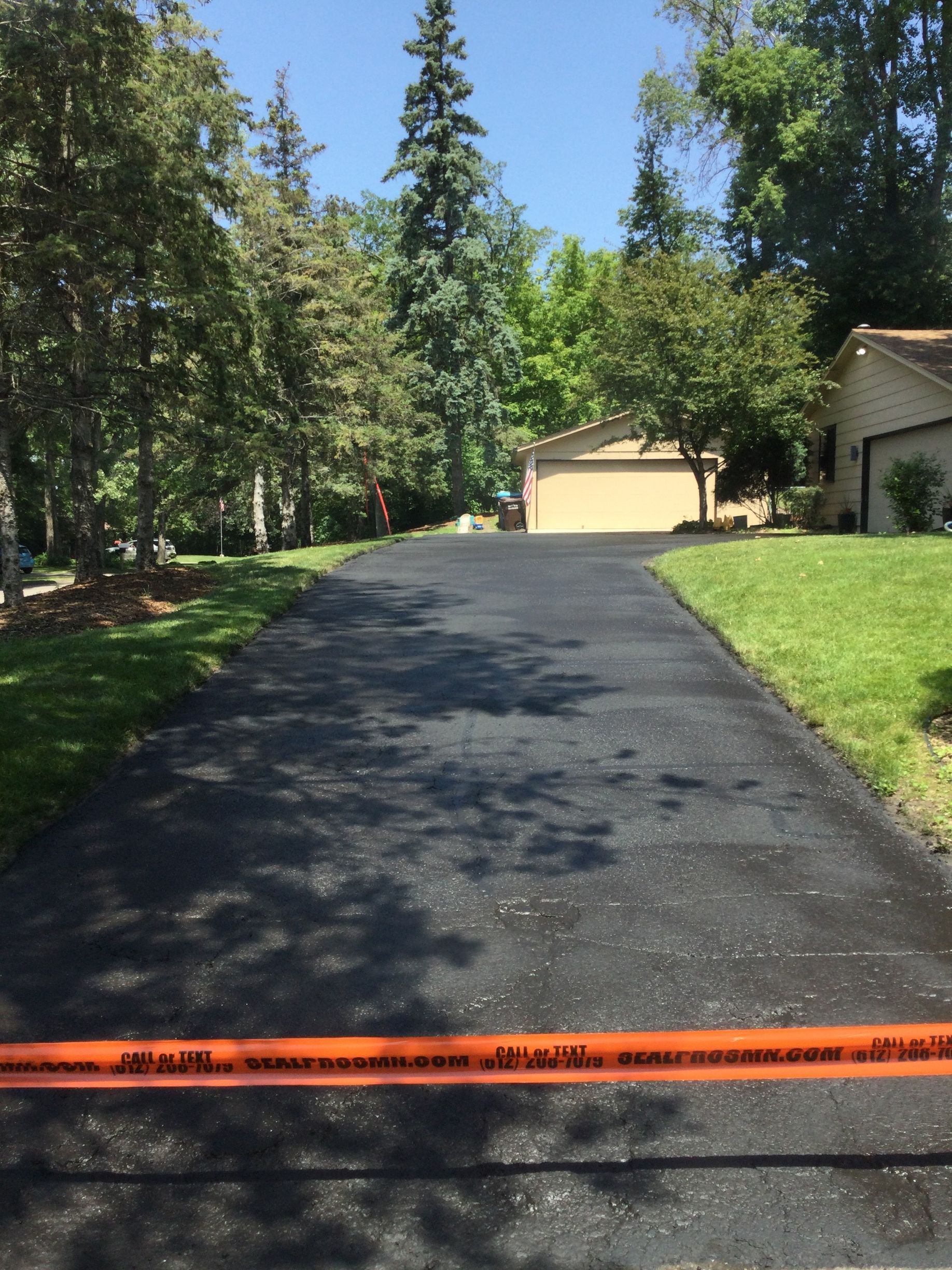 Newly paved asphalt driveway leading to a garage, orange caution tape in foreground.
