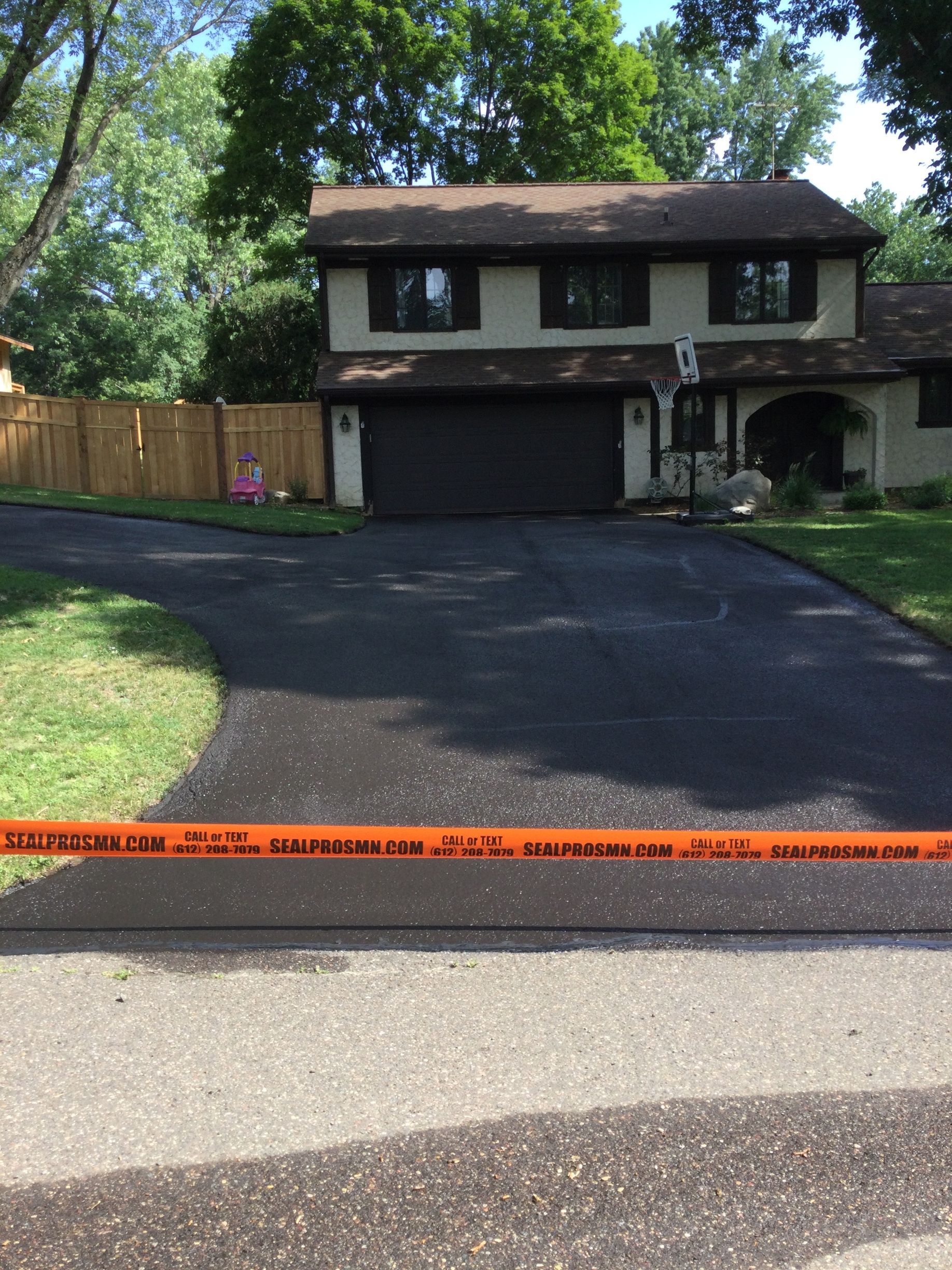 Paved driveway in front of a two-story house, orange caution tape in foreground.