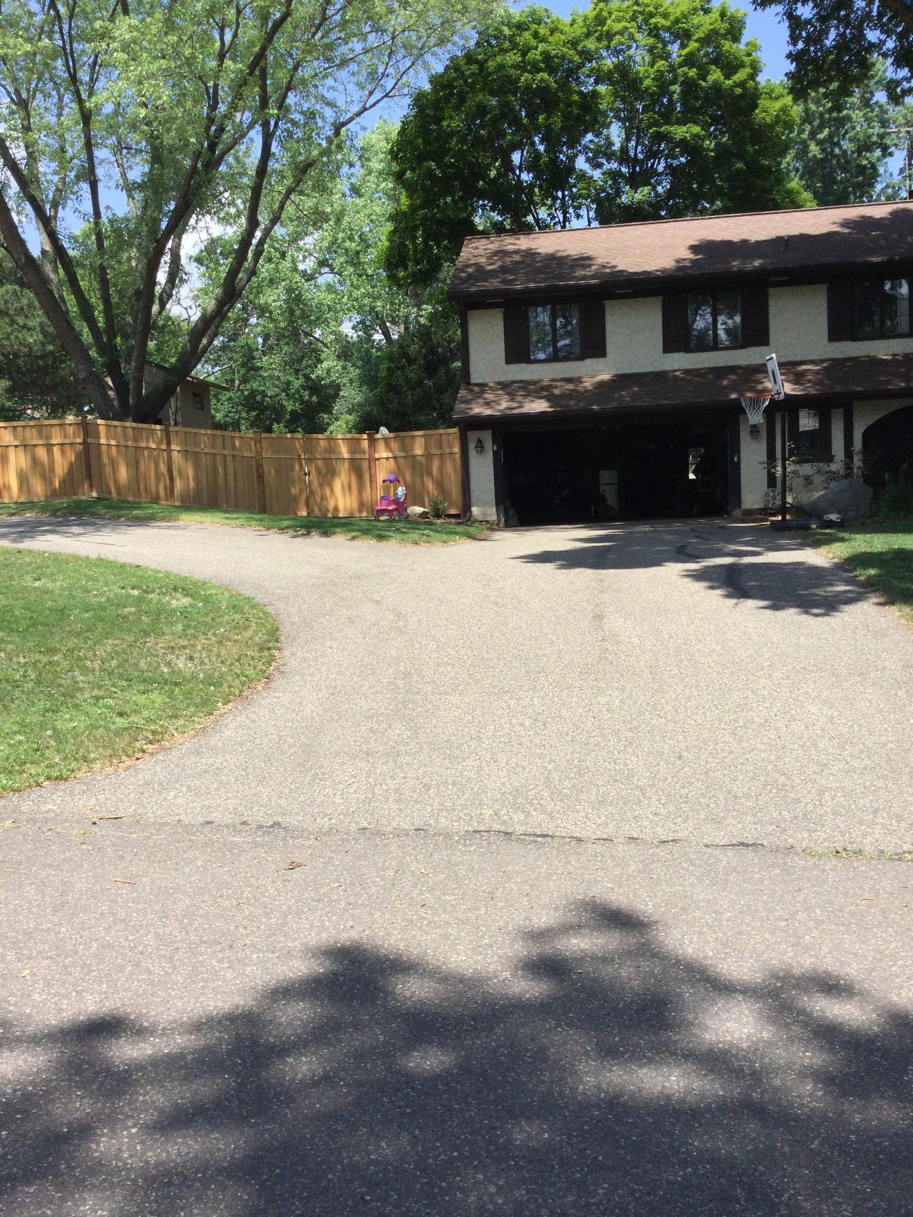 Driveway leading to a two-story house with a garage and a wooden fence in the background.