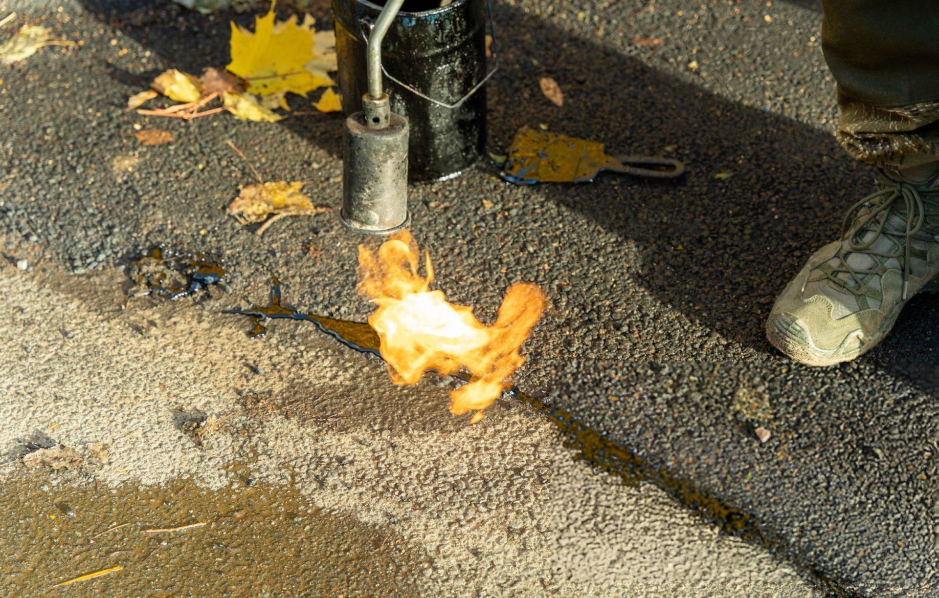 Worker using a gas burner to meticulously apply mastic sealant to cracks in an asphalt surface Worker using a gas burner to meticulously apply mastic sealant to cracks in an asphalt surface