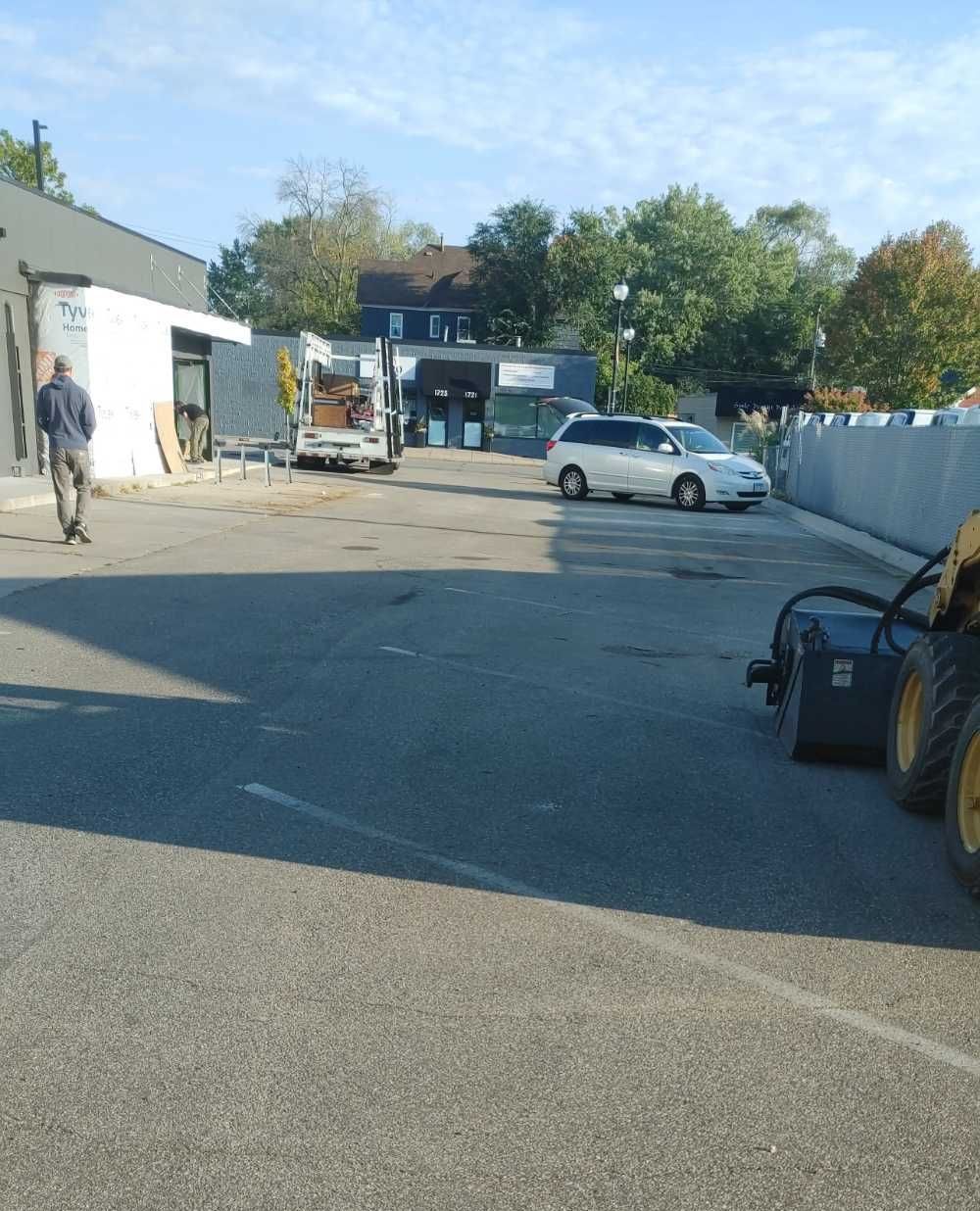 Man walking on asphalt toward building, van parked near storefront. Construction equipment present.