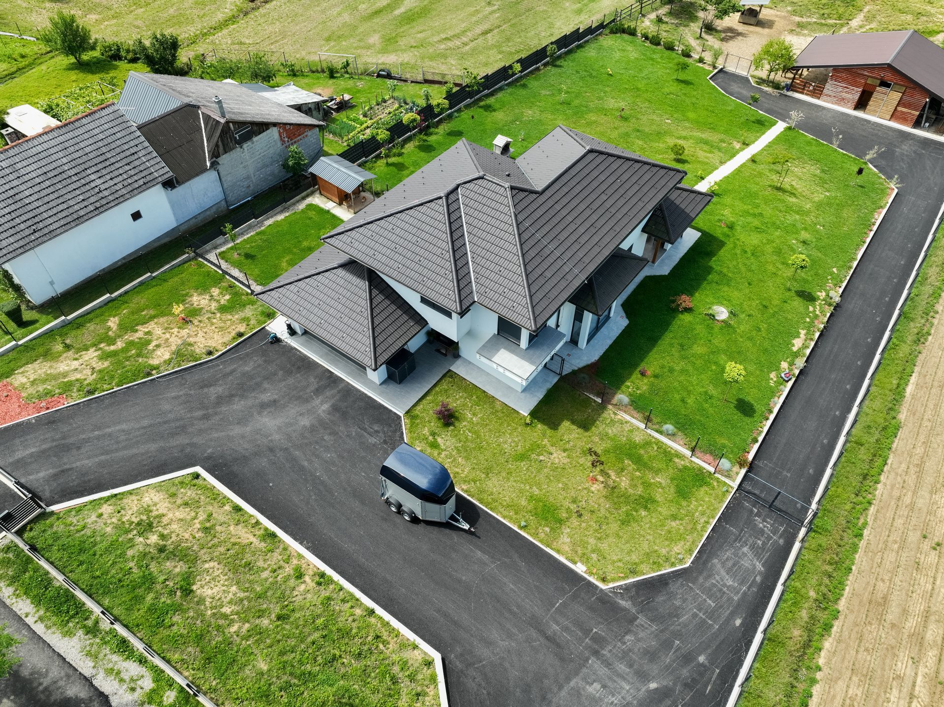 Flame heating and sealing a crack in asphalt pavement during road repair work. Aerial view of a modern minimalist house surrounded by an asphalted driveway.
