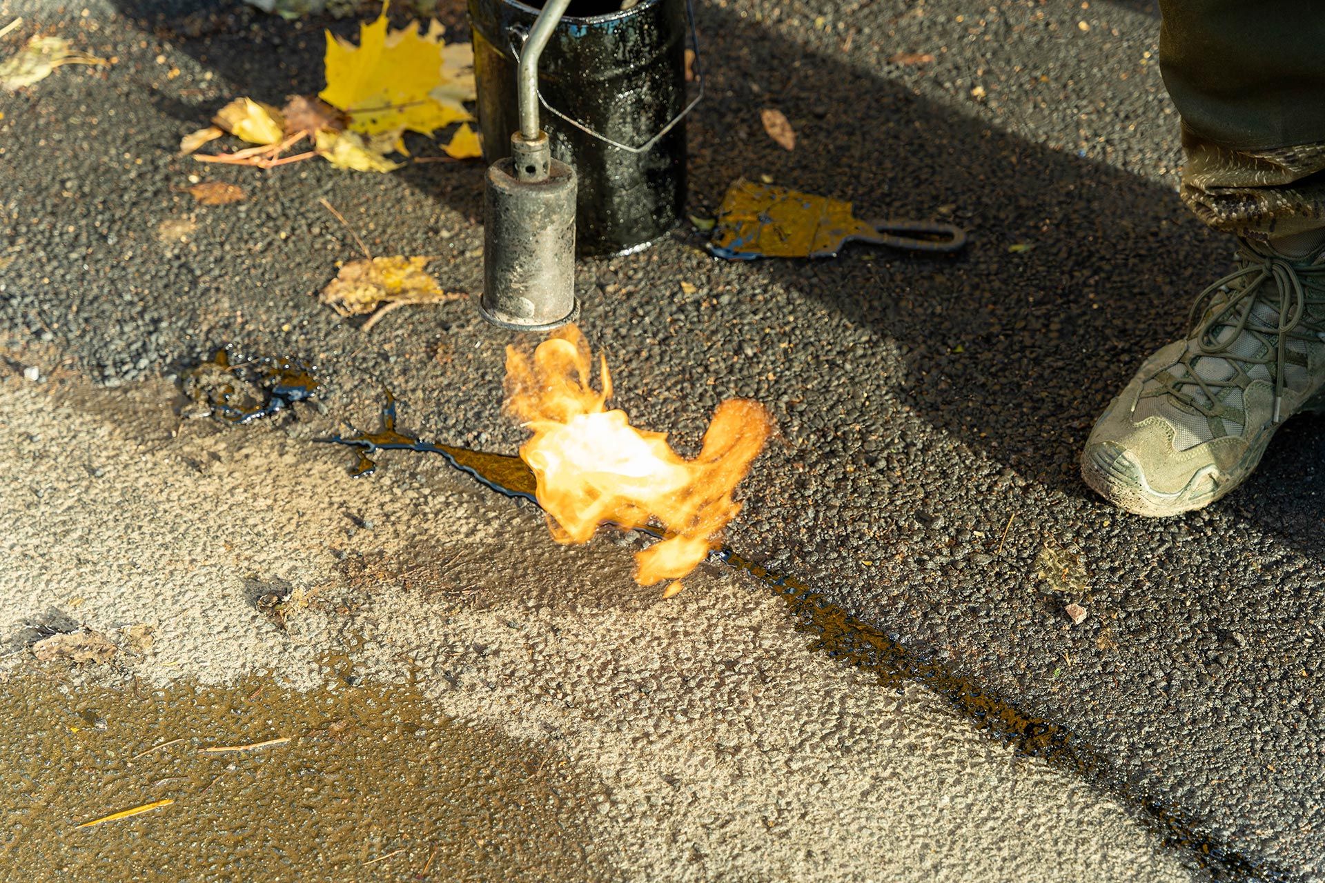 Flame heating and sealing a crack in asphalt pavement during road repair work. Flame heating and sealing a crack in asphalt pavement during road repair work.