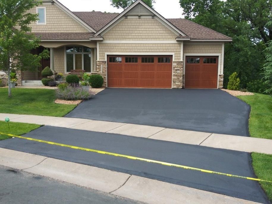 Black paved driveway in front of a house with brown garage doors.