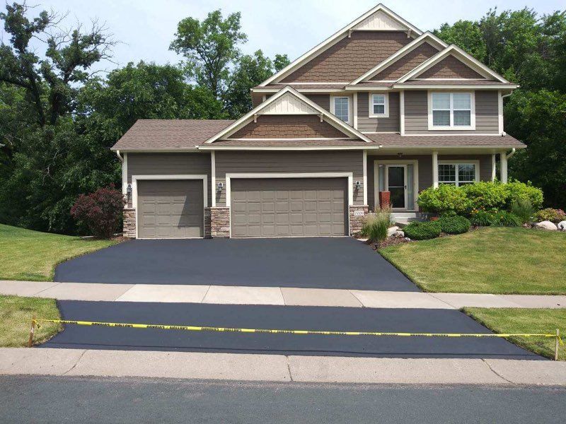 Two-story house with new black driveway; yellow caution tape across driveway entrance.