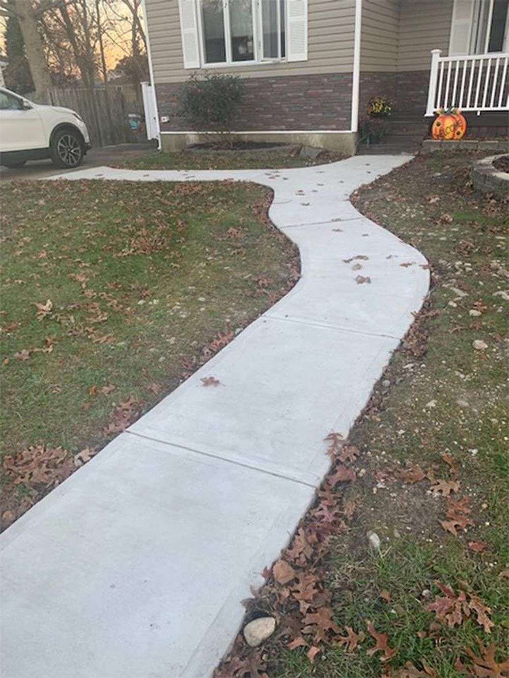 A winding concrete walkway leads to a beige house with a pumpkin decoration in autumn.