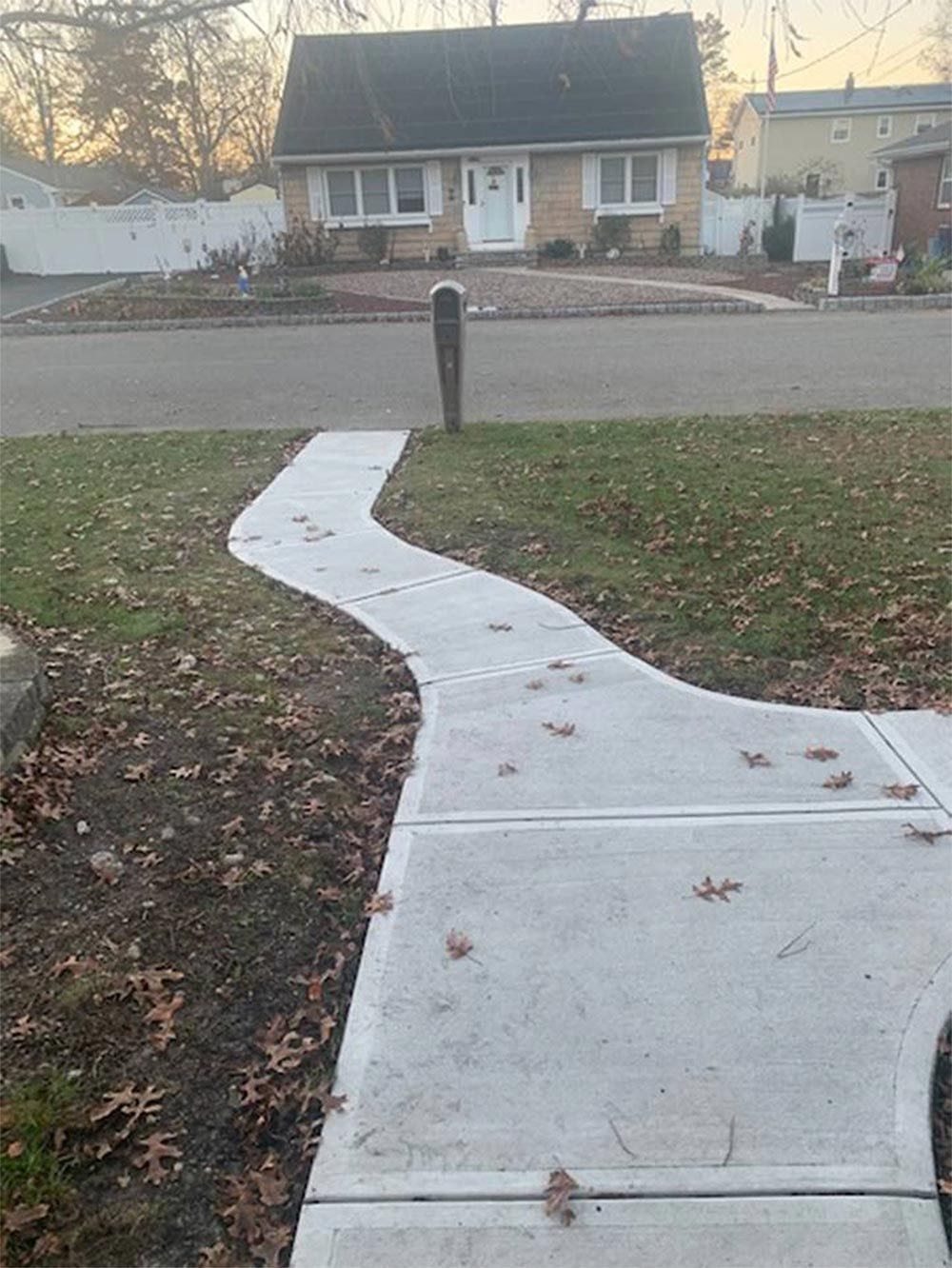 Concrete path curves toward a brick house with a white door and green roof on a sunny day.