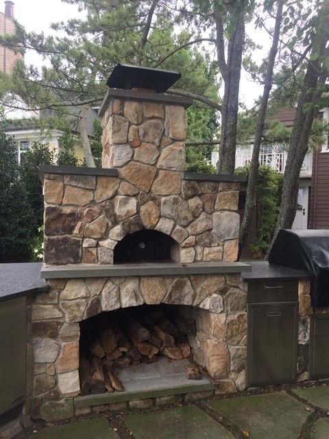 Stone outdoor pizza oven with wood storage below, surrounded by cabinetry.