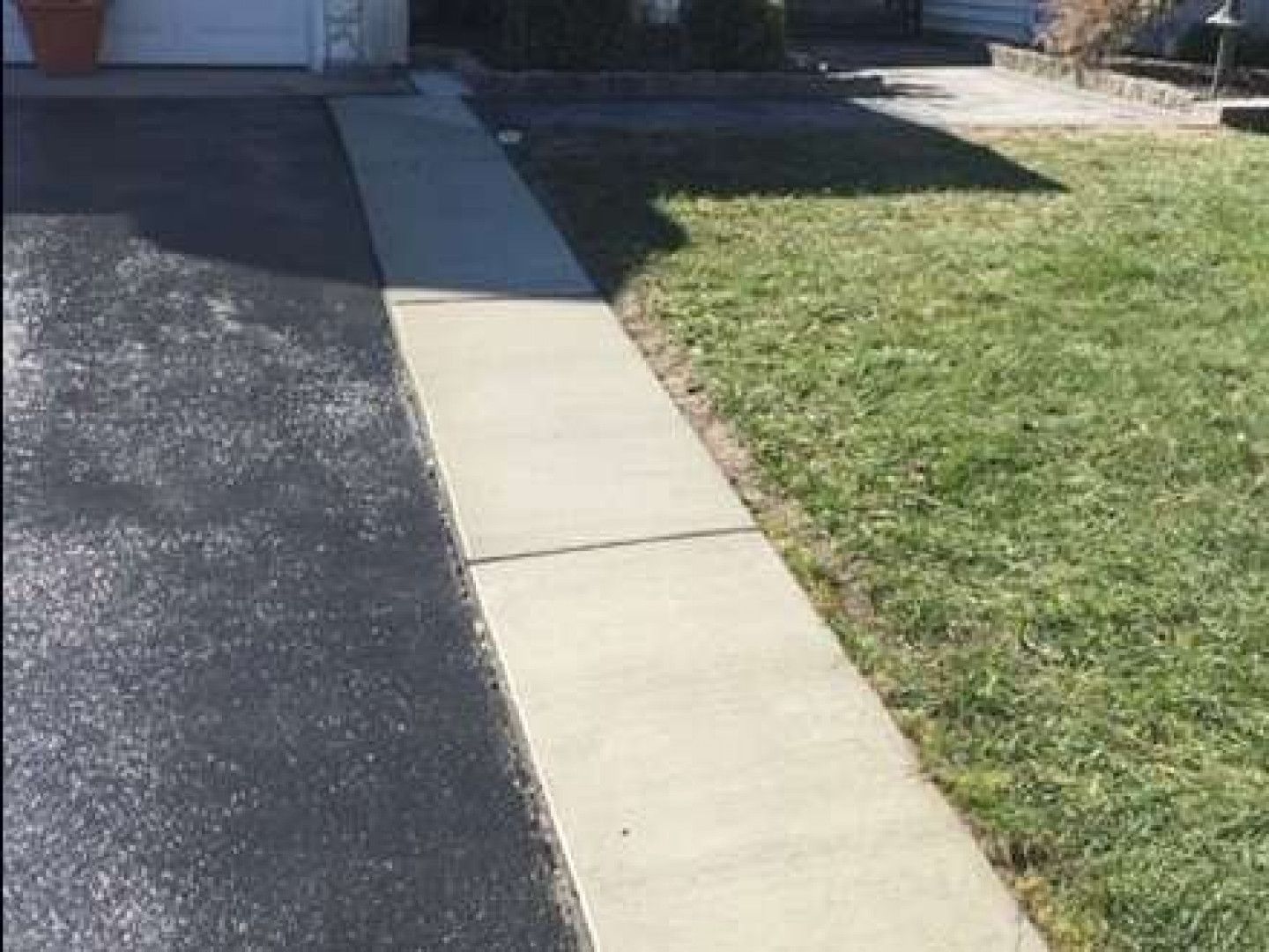 Asphalt driveway and concrete walkway beside a patch of grass.