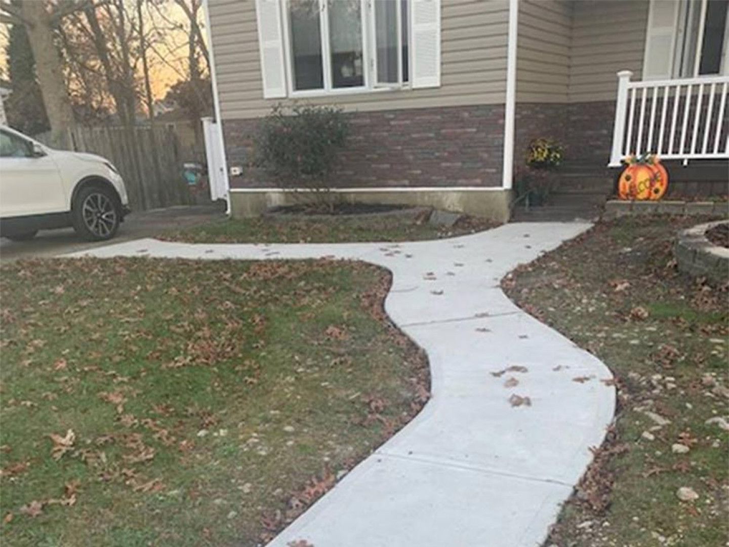 Concrete walkway leading to a house with a car parked to the left.