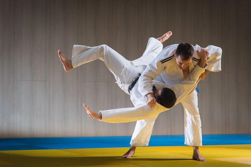 Two judo athletes in white gis mid-throw on a mat, one lifted horizontally in a training match