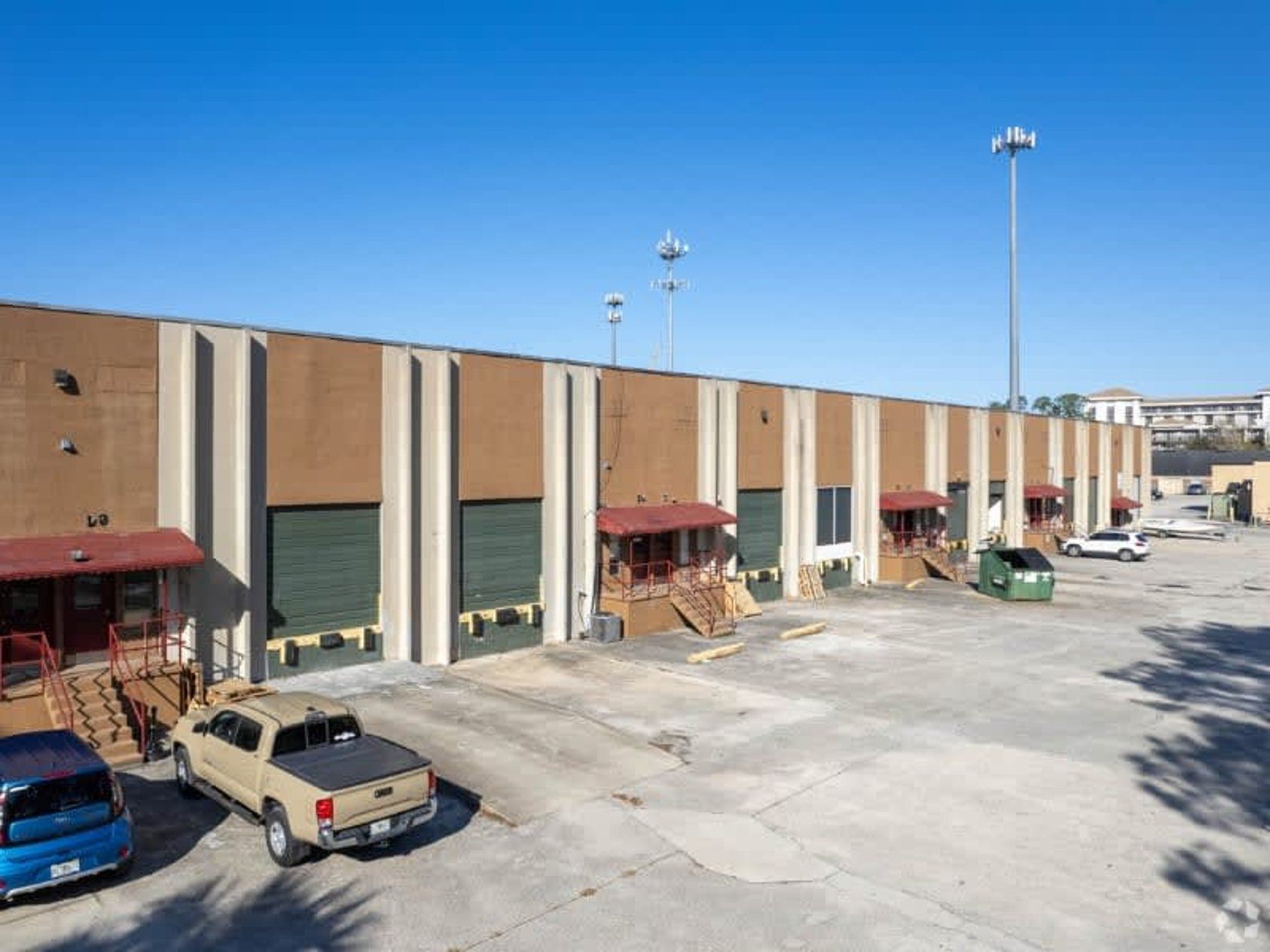 Exterior view of a warehouse building with multiple loading docks, vehicles in the parking area, and a clear sky.