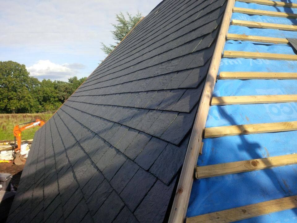Roof under construction with black shingles and exposed blue underlayment on one side