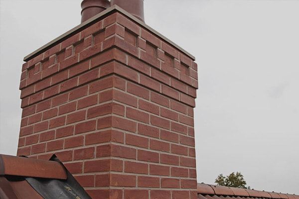 Red brick chimney with a metal cap against a cloudy sky.