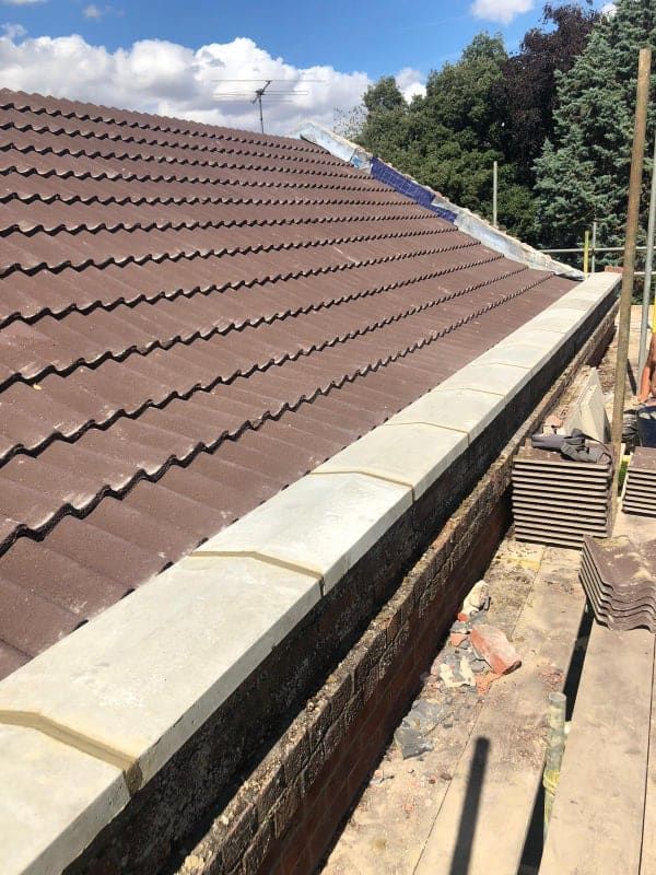 Brown tiled roof with white gutter along a house under a blue sky, viewed from a narrow side walkway