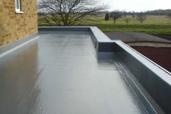Flat rooftop with a wet gray surface, low parapet, and a brick wall on the left under an overcast sky