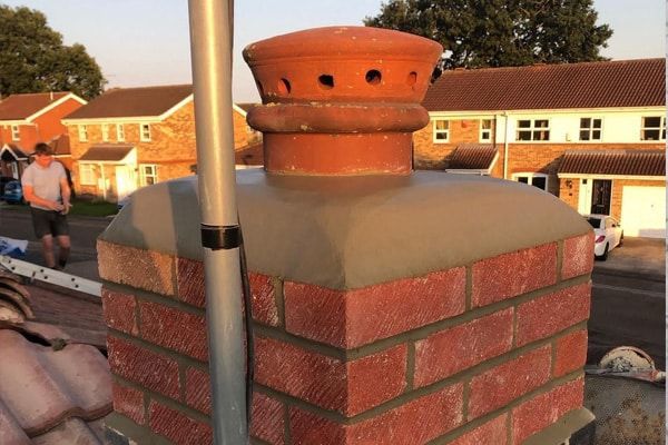 Brick rooftop chimney with terracotta vent cap at sunset, with school buildings in the background
