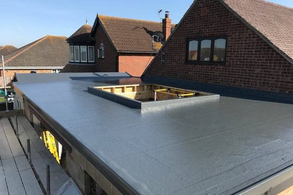 Flat gray rooftop with a skylight opening between brick houses under a clear sky