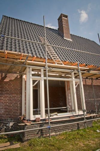 Brick house under renovation with scaffolding and a new roof under a blue sky