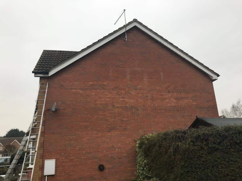 Side view of a red brick house with a ladder against it and a hedge in front