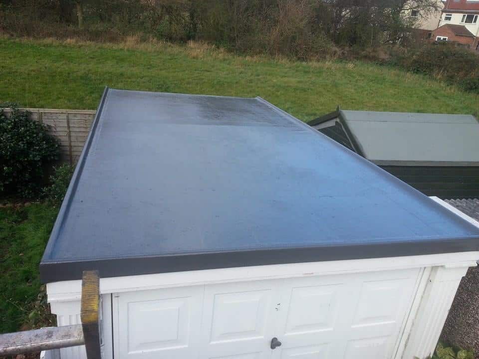 Blue flat roof over a white garage with a green yard in the background