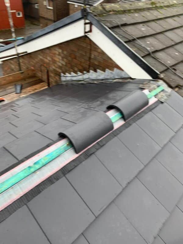 Roof repair on a slate roof with black underlayment and exposed green insulation near a dormer edge