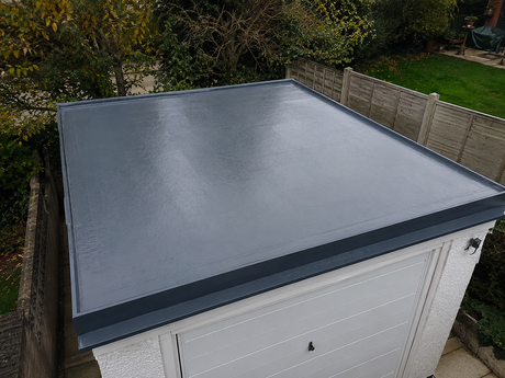 Flat gray metal roof on a garage, seen from above with trees and fencing around it