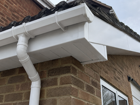 White gutter and downspout on a brick house roof corner with visible roof damage