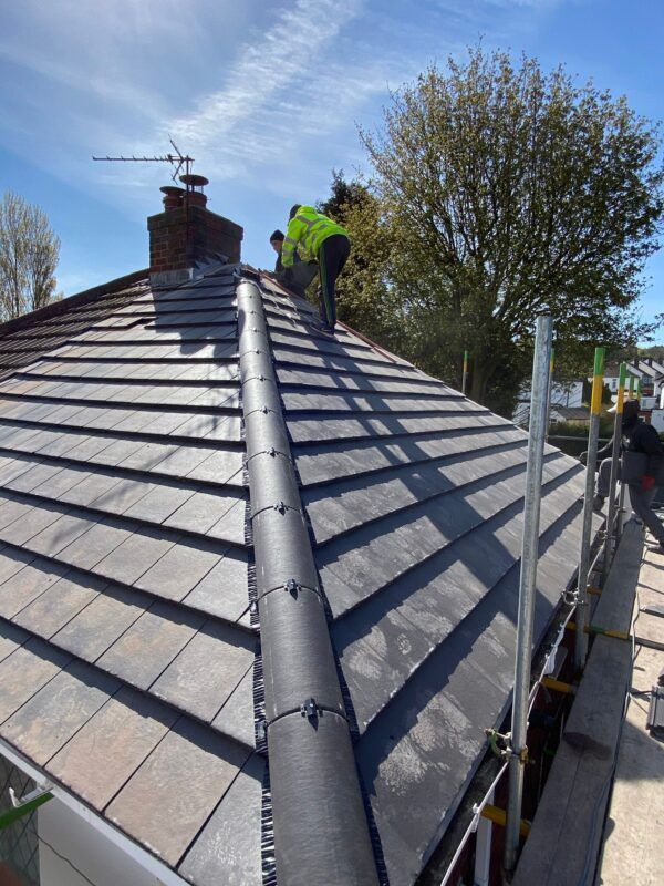 Workers installing a black roof vent on a gray tiled roof on a sunny day